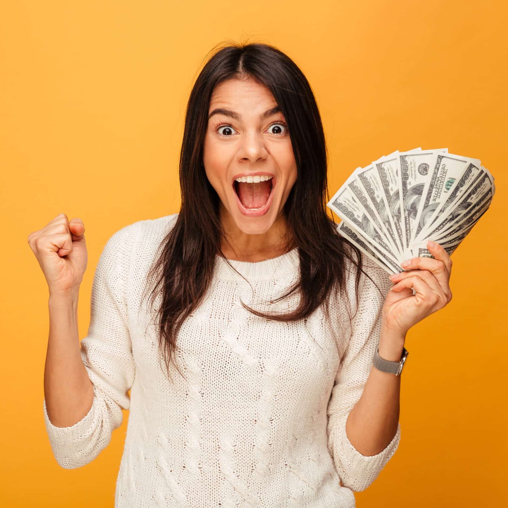 Portrait of an excited young woman holding money banknotes